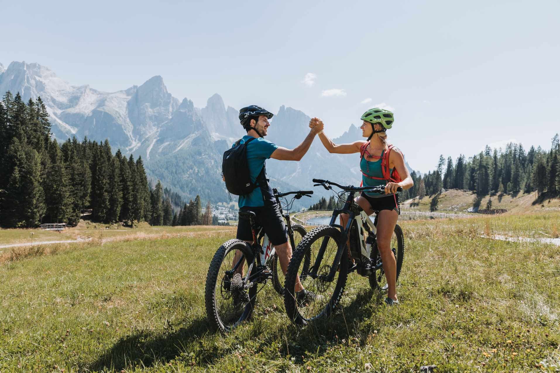 Due ciclisti si salutano con lo sfondo delle dolomiti